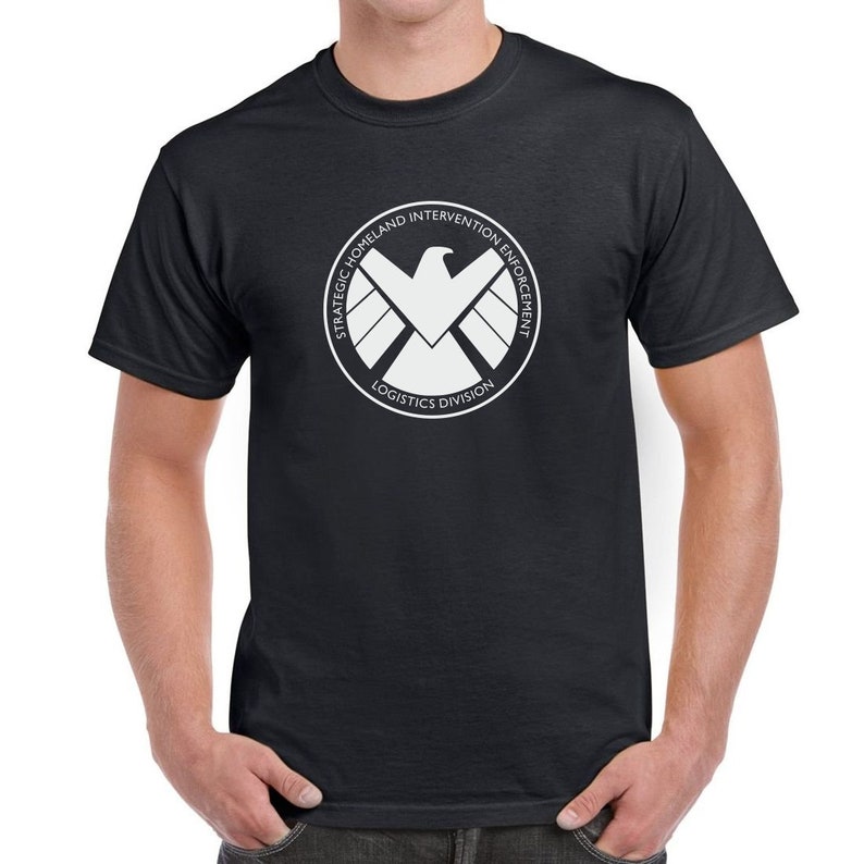 May include: Black t-shirt with a white logo of the Strategic Homeland Intervention Enforcement Logistics Division, also known as S.H.I.E.L.D., featuring a white eagle with wings spread and a circle around it.