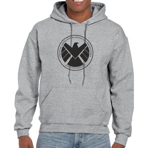 May include: A gray hooded sweatshirt with a black logo on the front. The logo is a circle with the words "Strategic Homeland Intervention Enforcement Logistics Division" around the outside and a black falcon inside.