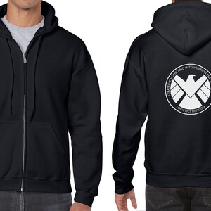 May include: Black zip-up hoodie with a white logo on the back. The logo is a circle with a white eagle inside and the text "Strategic Homeland Intervention Enforcement Logistics Division".