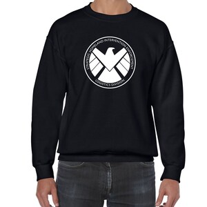 May include: Black sweatshirt with a white logo of the S.H.I.E.L.D. logo. The logo is a circle with the words "Strategic Homeland Intervention Enforcement Logistics Division" around the outside and a stylized eagle inside.