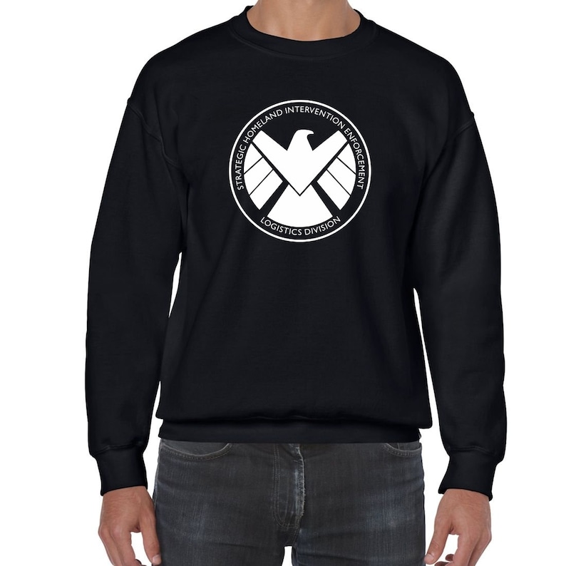 May include: Black sweatshirt with a white logo of the S.H.I.E.L.D. logo. The logo is a circle with the words "Strategic Homeland Intervention Enforcement Logistics Division" around the outside and a stylized eagle inside.