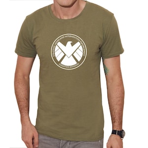 May include: A green t-shirt with a white logo featuring a shield with a bird inside. The logo reads "Strategic Homeland Intervention Enforcement Logistics Division".
