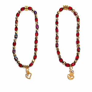 May include: Two beaded bracelets featuring alternating deep red translucent beads and metallic gold faceted beads. One bracelet includes a gold heart charm with a clear stone, while the other features a gold alien head charm with a clear stone.