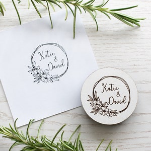 May include: A wooden stamp featuring a floral wreath design with the text "Katie & David" in a handwritten font.