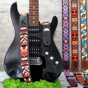 May include: Black electric guitar with a colorful patterned guitar strap. Three additional guitar straps with different patterns are shown in the background.