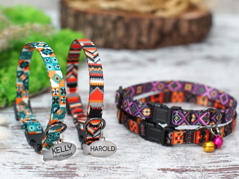 May include: Three colorful cat collars with adjustable buckles and breakaway safety clasps. The collars feature a geometric pattern in shades of orange, teal, purple, and black. Two of the collars have personalized name tags that read "KELLY I'm chipped" and "HAROLD". The third collar has a small bell attached.
