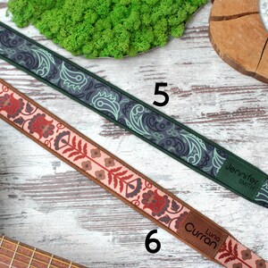 K&ouml;nnte beinhalten: Zwei Gitarrengurte mit unterschiedlichen Mustern. Ein Gurt ist gr&uuml;n und schwarz mit einem Paisley-Muster und dem Text "Jennifer Smith". Der andere Gurt ist rosa und braun mit einem Blumenmuster und dem Text "Luna Curran".