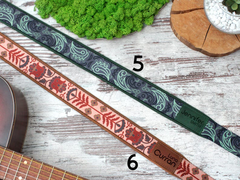 K&ouml;nnte beinhalten: Zwei Gitarrengurte mit unterschiedlichen Mustern. Ein Gurt ist gr&uuml;n und schwarz mit einem Paisley-Muster und dem Text "Jennifer Smith". Der andere Gurt ist rosa und braun mit einem Blumenmuster und dem Text "Luna Curran".