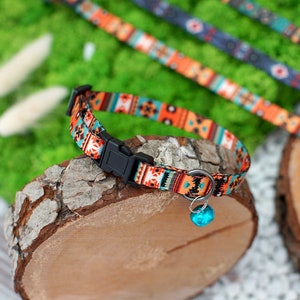 May include: A close-up of a colorful cat collar with a geometric pattern in shades of orange, blue, and black. The collar has a black buckle and a turquoise bell.