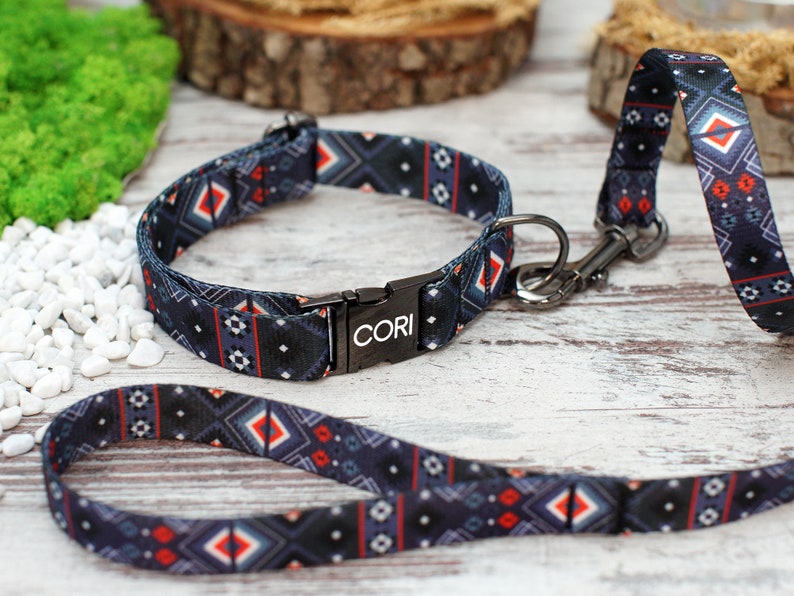 K&ouml;nnte beinhalten: Ein schwarzes und blaues Hundehalsband und eine Leine mit geometrischem Muster. Das Halsband hat eine schwarze Metallschnalle mit dem eingravierten Wort "CORI".