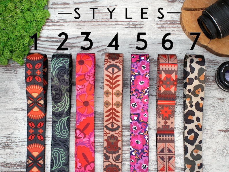 May include: Seven different styles of camera straps, numbered 1 through 7. The straps are made of fabric and feature various colourful patterns, including geometric, floral, and animal print designs.