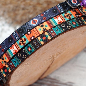 May include: Three colourful patterned cat collars with a bell on each. The collars are layered on top of each other and have a geometric design.