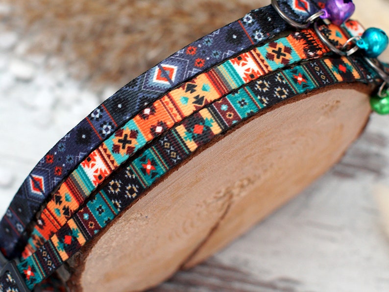 May include: Three colourful patterned cat collars with a bell on each. The collars are layered on top of each other and have a geometric design.