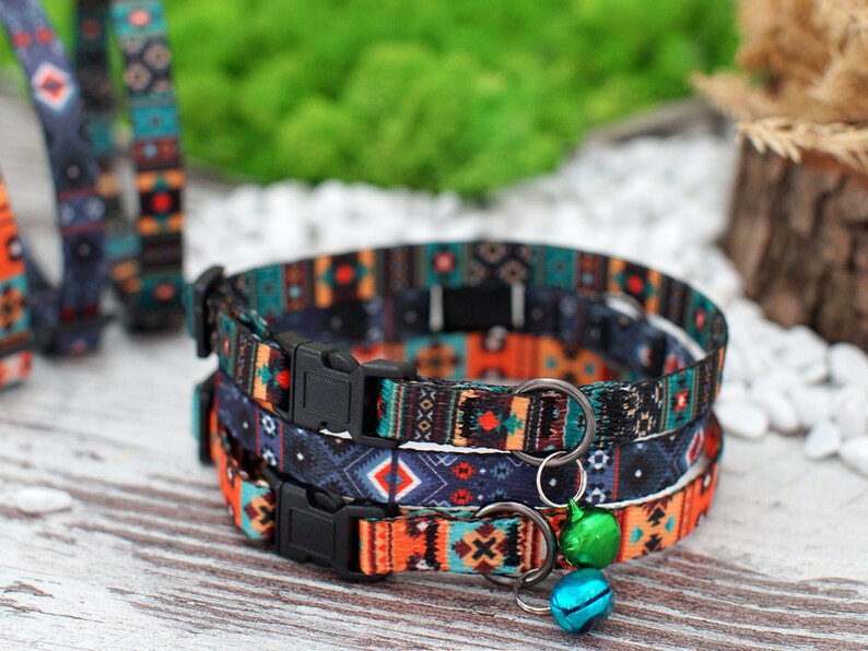 May include: Three colorful cat collars with a geometric pattern in shades of blue, orange, and black. The collars have adjustable buckles and a small bell charm.
