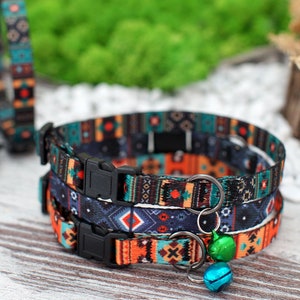 May include: Three colourful cat collars with a geometric pattern in shades of blue, orange, and black. The collars have adjustable buckles and a small bell charm.