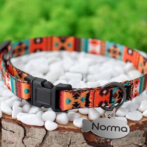 May include: A colorful cat collar with a geometric pattern in shades of orange, blue, and green. The collar has a black buckle and a silver tag that reads "Norma".