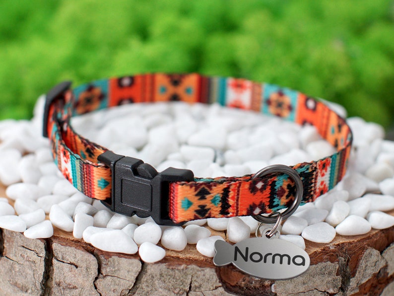 May include: A colorful cat collar with a geometric pattern in shades of orange, blue, and green. The collar has a black buckle and a silver tag that reads "Norma".