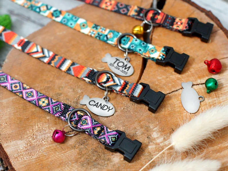 May include: Four colorful dog collars with adjustable buckles and metal fish-shaped tags. The tags are engraved with the names "TOM", "CANDY", and two blank tags. Each collar has a bell attached.