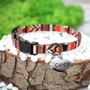May include: A colorful cat collar with a geometric pattern in orange, black, white, and gray. The collar has a black plastic buckle and a silver metal tag that says "CANDY".