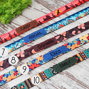 May include: A selection of colorful dog collars with personalized name tags. Designs include desert landscapes, floral patterns, and geometric prints. Each collar features a different name: Daisy, Abigail, Danielle, Eliza, and Emily.