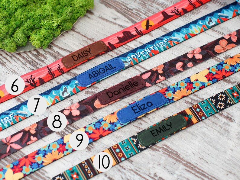 May include: A selection of colorful dog collars with personalized name tags. Designs include desert landscapes, floral patterns, and geometric prints. Each collar features a different name: Daisy, Abigail, Danielle, Eliza, and Emily.
