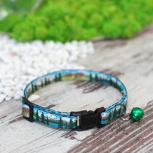 May include: A blue and green cat collar with a black buckle and a green bell. The collar features a printed design of a mountain scene.