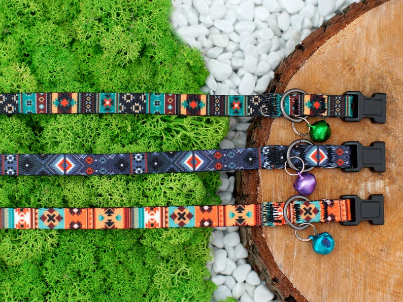 May include: Three colorful patterned dog collars with bell charms. The collars are black, blue, and orange with geometric designs. The bells are green, purple, and silver.