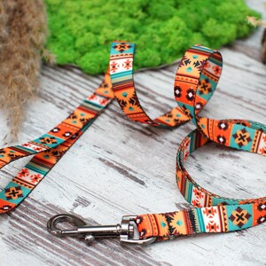 K&ouml;nnte beinhalten: Eine bunte Hundeleine mit einem geometrischen Muster in Orange-, T&uuml;rkis- und Braunt&ouml;nen. Die Leine hat einen silbernen Metallclip.