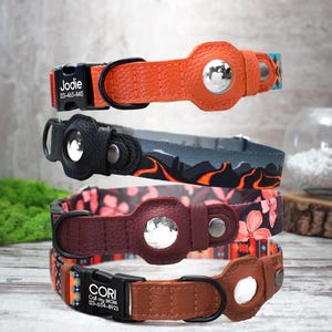 Peut inclure: Quatre colliers pour chien empil&eacute;s les uns sur les autres. Les colliers sont en cuir et pr&eacute;sentent diff&eacute;rents motifs et couleurs. Le collier du haut est orange avec une boucle noire et le texte "Jodie 123-456-8465". Le deuxi&egrave;me collier est noir avec un motif gris et orange. Le troisi&egrave;me collier est bordeaux avec un motif floral. Le collier du bas est marron avec un motif color&eacute; et le texte "CORI Call my MOM 123-456-8923".