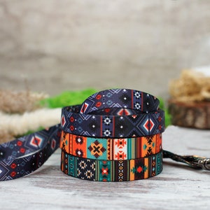 K&ouml;nnte beinhalten: Eine bunte Hundeleine mit einem geometrischen Muster in Blaut&ouml;nen, Orange, Gr&uuml;n und Wei&szlig;. Die Leine hat einen silbernen Metallclip.