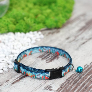 May include: A blue and orange patterned cat collar with a black buckle and a small blue bell.