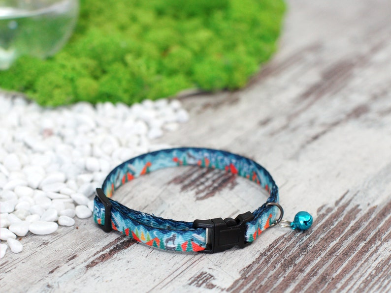 May include: A blue and orange patterned cat collar with a black buckle and a small blue bell.