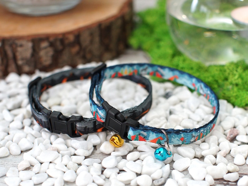 May include: Two colourful cat collars with bells. One collar is black with orange and white accents, the other is blue with orange and white accents. Both collars have black plastic buckles.