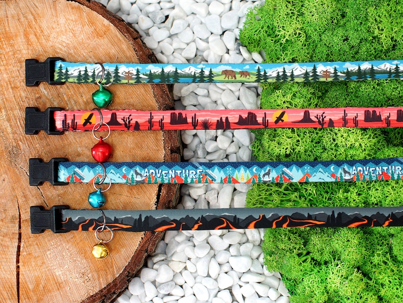 May include: Four colourful cat collars with different nature-themed patterns and bell charms. The collars feature designs such as mountains, cacti, and a wolf howling at the moon. The collars are made from durable, adjustable webbing.