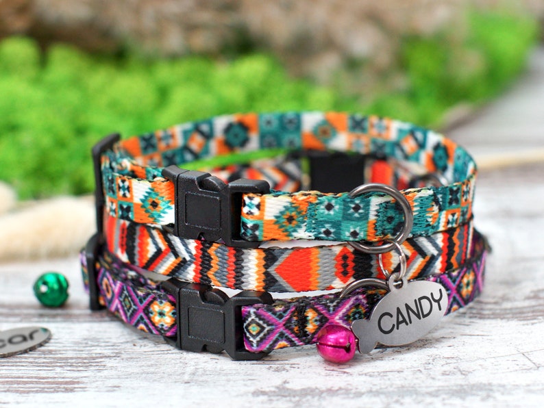 Op de afbeelding: Drie kleurrijke kattenhalsbanden met geometrische patronen. De halsbanden liggen op elkaar. De bovenste halsband is turquoise, wit en oranje. De middelste halsband is oranje, grijs en zwart. De onderste halsband is paars, roze en zwart. Elke halsband heeft een zwarte plastic gesp en een zilveren metalen ring. De onderste halsband heeft een roze bel en een zilveren label met de tekst "CANDY".