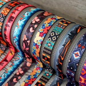 May include: A selection of patterned dog collars in various designs. The collars display floral, geometric, and landscape patterns. The collars are rolled up, displaying a range of colours and designs, suitable for pets.