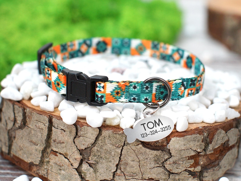 May include: A colorful patterned dog collar with a black buckle and a silver fish-shaped tag that reads "TOM 123-324-3255".