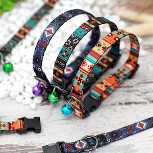 May include: Three colourful cat collars with geometric patterns and bell charms. The collars are made of a soft, woven fabric and feature a black plastic buckle.