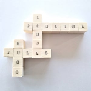 May include: Wooden blocks spelling out the names "Jules" and "Pauline" in a crossword puzzle format.