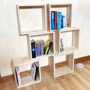 Peut inclure: Un ensemble de six étagères en bois, disposées en quinconce, avec des livres sur certaines des étagères. Les étagères sont en bois naturel et ont un aspect rustique.