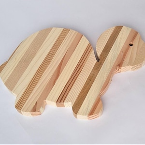 Może przedstawiać: Drewniana deska do krojenia w kształcie żółwia. Deska wykonana jest z wielu pasków drewna, tworząc wzór w paski. Żółw ma mały otwór w głowie.