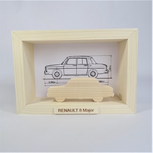 Könnte beinhalten: Eine Holz-Schattenbox mit einem ausgeschnittenen Holzauto im Inneren. Das Auto ist ein Renault 8 Major. Die Box hat einen weißen Hintergrund mit einer Strichzeichnung des Autos mit Maßen in Metern.