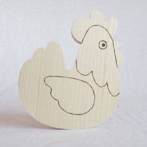 Może przedstawiać: Nieukończona drewniana figurka kurczaka z prostym zarysowaniem cech ptaka. Kurczak jest jasnobrązowy i ma duże, zaokrąglone ciało.