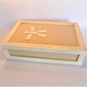 Puede incluir: Una caja de madera con una tapa de color marrón claro. La tapa tiene un diseño simple de figura de palo hecho con pequeños bloques de madera.