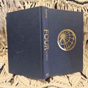 May include: A navy blue hardback book titled "FOUR" with gold lettering and a gold graphic of a Ferris wheel and globe. The spine reads "ROTH" and "Divergent Collection".