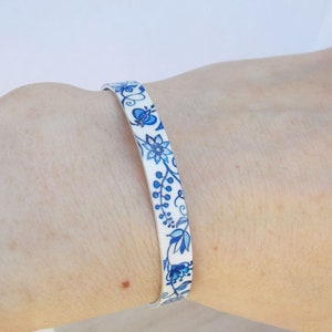 Puede incluir: Un brazalete blanco con un patrón floral azul y blanco.