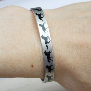 May include: A silver bracelet with a black silhouette of a horse design. The bracelet is worn on a person's wrist.