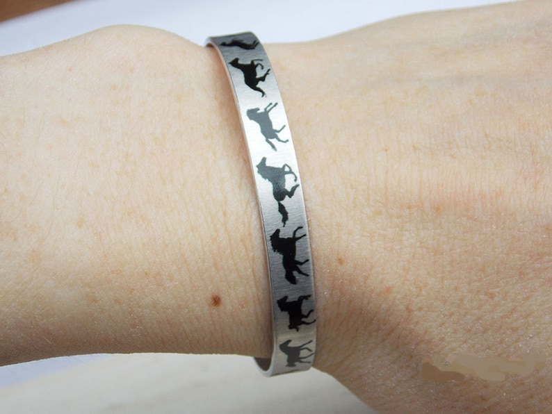 May include: A silver bracelet with a black silhouette of a horse design. The bracelet is worn on a person's wrist.