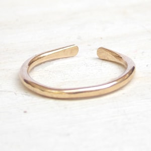May include: A simple gold ring with a hammered finish. The ring is open and has a slightly curved shape.