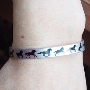 May include: A silver bracelet with a row of black horse silhouettes running around the band.
